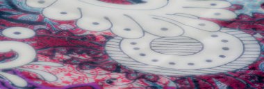 Karmaşık desenler ve canlı renkler içeren canlı kumaşın yakın plan görüntüsü. Katlar ve doku zarif tasarıma derinlik ekler.