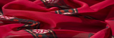 Kırmızı, turuncu ve koyu yeşil renklere sahip canlı kumaşın bulanık görüntüsü. Hassas dokular ve parlak detaylarla karışık çiçek ve geometrik desenler içeriyor..