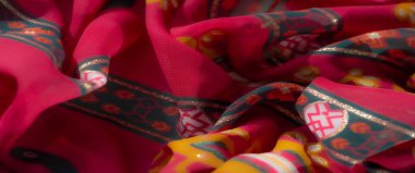 Görüntü, dinamik pembe ve turuncu kumaş, geometrik ve çiçek desenli, ince yeşil aksanlı. Malzemeler ayrıntılı dokular ve zarif kıvrımlar sergiliyor.