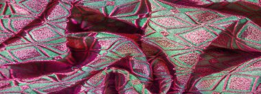 Çarpıcı pembe geometrik nakışlarla süslenmiş canlı yeşil bir kumaşın bulanık görüntüsü, pürüzsüz kıvrımlar ayrıntılı tasarımı ortaya çıkarıyor. Kumaş zengin yaratıyor.,