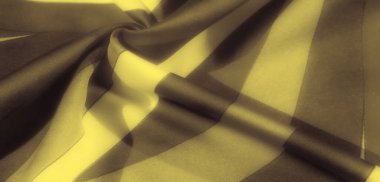 Lükslü sarı kumaşlar koyu siyah çizgilerle sarmalanmış yumuşak kıvrımlar ve gölgeler oluşturuyor. Doku ışığı yakalar, pürüzsüz, görsel olarak çekici bir eğim yaratır..