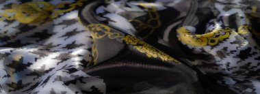 Şeffaf siyah ve beyaz tekstil ile altın zincir desenlerinin sanatsal karışımını bulanıklaştırarak, doku ve zarafetin kusursuz bir etkileşimini oluşturur..