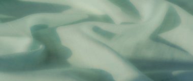 Karmaşık şebeke detaylarıyla yumuşakça katlanmış yeşil kumaş. Hassas tasarım ve pürüzsüz doku, zarif ve sofistike bir tonda yayılır..