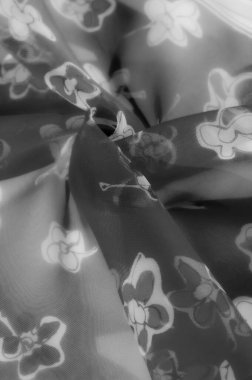 Gri tonda yarı şeffaf kumaş, sanatsal çiçek motifleriyle süslenmiş. Yumuşak, akışkan kıvrımlar zarif bir zarafet yayıyor, minimalist tasarımlar için mükemmel..