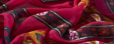 Kırmızı ve turuncu renkli koyu çiçek desenleri olan katlanmış bir kumaşın bulanıklığı, yeşil ve siyah geometrik motiflerle vurgulanmış ve altın renkli parlak ışıklar..