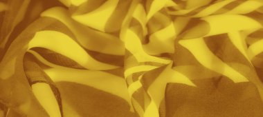 Girdap şeklinde kahverengi aksanlı bulanık sarı kumaş: Açıklama: Dinamik bir şekilde katlanmış kıvrımlı kahverengi aksanlı canlı sarı kumaşın bulanıklığı,