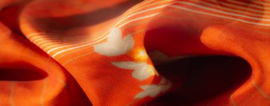 Karmaşık çiçek aksanları ve dinamik beyaz çizgileri olan bulanık turuncu kumaş sanatsal veya yaratıcı tasarım uygulamaları için ideal canlı bir doku sergiliyor..