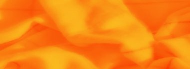 Yumuşak girdaplı ve eğimli turuncu kumaşın bulanık hali sarıya dönüşüyor ve görsel olarak çekici bir tekstil parçası oluşturuyor..