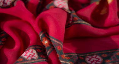 Görüntü, altın ve yeşil aksanlarla bezenmiş parlak kırmızı bir kumaşın karmaşık tasarımını yakalar. Çiçeksel ve geometrik desenler ve parıltılı detaylarla vurgulanır..