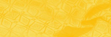 İnce geometrik desenli yumuşak sarı kumaşın bulanık dokusu. Kumaşın kıvrımları pürüzsüz, akıcı bir görünüm yaratıyor, zarif bir parıltı ve tasarımın altını çizen karmaşık bir detay sergiliyor..