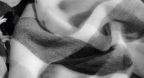 Görüntü, gri tonlu bir kumaşın dinamik kıvrımlarını ve hassas dokularını yakalar. Işığın yüzeyinde çok az ama rafine bir tasarım için ustaca oynadığı bir yer..
