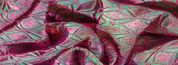 Çarpıcı pembe geometrik nakışlarla süslenmiş canlı yeşil bir kumaşın bulanık görüntüsü, pürüzsüz kıvrımlar ayrıntılı tasarımı ortaya çıkarıyor. Kumaş zengin yaratıyor.,