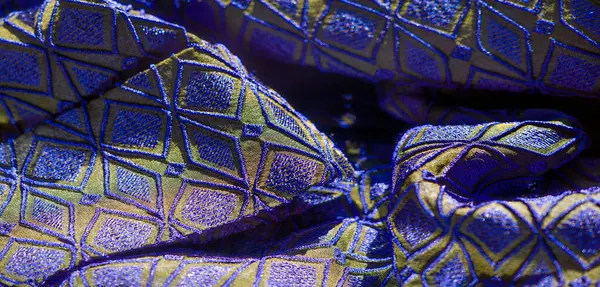 Görüntü, kumaşın mavi ve altın renkleri üzerinde güzel bir etkileşim geometrik elmas desenler, karmaşık nakış ve yumuşak, sanatsal kıvrımlar.