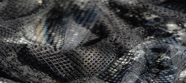 Karmaşık ızgara benzeri detaylarla siyah dantelli kumaşın bulanık görüntüsü ve parıldayan ışık yansımaları, materyalin zarafetini ve inceliğini vurguluyor.