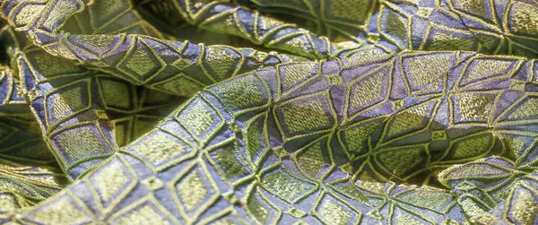 Görüntü, katmanlı elmas desenli, işlemeli yeşil ve mavi bir tekstil üzerine odaklanır. Sanatsal ustalığı ve parıldayan metal aksanını gösterir..