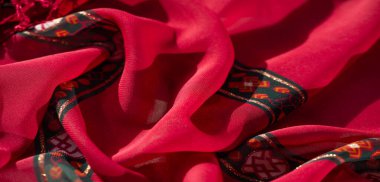 Renkli kumaşın bulanık yakın plan görüntüsü sarı çiçekli elementler ve koyu kırmızı ve yeşil aksanlar. Karmaşık detaylar tekstil tasarımını canlandırır.