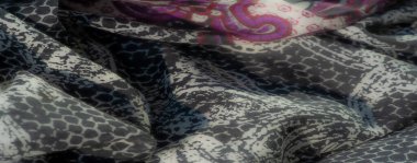 Kırmızı, mor ve mavinin canlı tonlarında, karmaşık çiçek desenleri içeren canlı bir kumaşın bulanıklığı dinamik ve zarif bir tasarım yaratıyor..