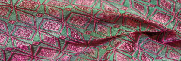 Pürüzsüz, katlanmış, parlak yeşil ve pembe geometrik nakışlı bulanık bir kumaş. Şablonun ince dokusu ve karmaşık detayları görüntüye derinlik ve lüks görsel cazibe ekler..