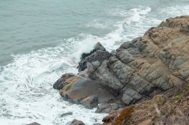 Pasifik Okyanusu 'nun güzel dalgaları kayalık kıyılara, yakın çekim pastel renklerine vurur.