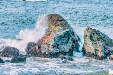 Su sıçrıyor. Kristal berrak deniz suyu kayalara çarpıyor. Deniz dalgaları okyanusun taştan kıyılarında kırılır, mavi su pastel renklerde.