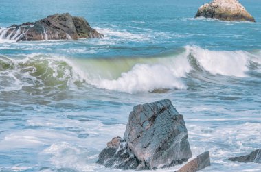 Dalga yakın planda sıçrıyor. Kristal berrak deniz suyu okyanusta, San Francisco Körfezi 'nde kaya oluşumlarına çarpar. Mavi su, pastel renkler..