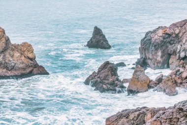 Okyanusun ham gücü ve güzelliği, yakın çekim, kayalık deniz kayalıkları, Pasifik Körfezi 'nin güzel dramatik deniz manzarası, Kaliforniya, ABD. Kayaların kaba dokusu, suyun akışkanlığıyla çelişiyor. Huşu hissi uyandırıyor ve merak uyandırıyor..