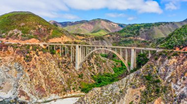 Kaliforniya Otoyolu 1 'deki Bixby Creek Köprüsü' nün çarpıcı manzarası. Köprü, pitoresk uçurumların ve turkuaz Pasifik sularının üzerine uzanarak eşsiz bir manzara ve seyahat atmosferi yaratır..