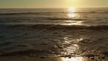 Kumsalda altın gün batımı, köpüklü dalgalar beyaz kumsala doğru yuvarlanıyor güneş ışığı altında