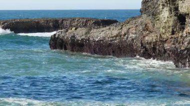 Güneş doğarken okyanus dalgaları kayalara çarpıyor.