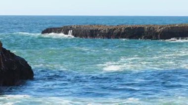 Güneş doğarken okyanus dalgaları kayalara çarpıyor.