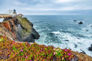 San Francisco, Kaliforniya yakınlarındaki Point Bonita Deniz Feneri Pasifik Okyanusu üzerindeki engebeli bir uçurumun üzerinde duruyor. Üzerinde paslı bir fener kulesi ve bulutlu bir gökyüzünün altındaki tarihi asma köprü bulunuyor.