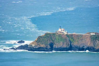 San Francisco, Kaliforniya yakınlarındaki Point Bonita Deniz Feneri Pasifik Okyanusu üzerindeki engebeli bir uçurumun üzerinde duruyor. Üzerinde paslı bir fener kulesi ve bulutlu bir gökyüzünün altındaki tarihi asma köprü bulunuyor.