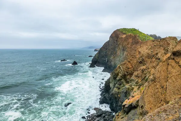 San Francisco, Kaliforniya yakınlarındaki Point Bonita Deniz Feneri Pasifik Okyanusu üzerindeki engebeli bir uçurumun üzerinde duruyor. Üzerinde paslı bir fener kulesi ve bulutlu bir gökyüzünün altındaki tarihi asma köprü bulunuyor.