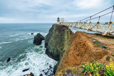 San Francisco, Kaliforniya yakınlarındaki Point Bonita Deniz Feneri Pasifik Okyanusu üzerindeki engebeli bir uçurumun üzerinde duruyor. Üzerinde paslı bir fener kulesi ve bulutlu bir gökyüzünün altındaki tarihi asma köprü bulunuyor.