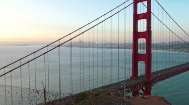 Golden Gate Köprüsü, gündoğumunda arka planda San Francisco şehir merkezi silueti olacak. Yumuşak sabah ışığında ikonik Kaliforniya manzarası, huzurlu okyanus ve berrak gökyüzü.