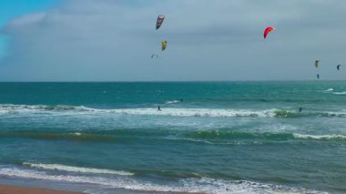 Uçurtmacılar 1. Otoyol boyunca Pacifica, California yakınlarında okyanus dalgalarına binerler. Renkli uçurtmalar bu hareketli kıyı sahnesinde turkuaz denizin üzerindeki bulutlu gökyüzünü dolduruyor.