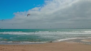 Kaliforniya, ABD - 24 Mayıs 2025, uçurtmacılar 1. Otoyol boyunca Pacifica, California yakınlarında okyanus dalgalarına biniyorlar. Renkli uçurtmalar bu hareketli kıyı sahnesinde turkuaz denizin üzerindeki bulutlu gökyüzünü dolduruyor.