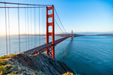 Golden Gate Köprüsü, San Francisco, California 'da gün doğumunda. Yumuşak pastel gökyüzü, sakin körfez suları ve ikonik kırmızı mimarisi olan Battery Spencer 'dan manzara. Huzurlu seyahat manzarası.
