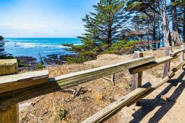 Okyanusa bakan kıyı şeridi boyunca tahta çitler var. Parlak ve huzurlu deniz manzarası kumlu yol, aşınmış ahşap ve yumuşak mavi su. Seyahat, doğa ve farkındalık temaları için ideal