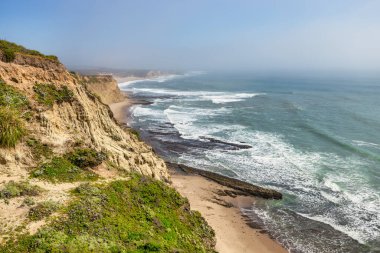 Dalgalar California 'da 1. Otoyol yakınlarındaki engebeli Pasifik Sahili boyunca yontulmuş kumtaşı kayalıklarına ve deniz mağaralarına çarpar. Kayalıkların eteklerinde küçük gizli bir sahil var.