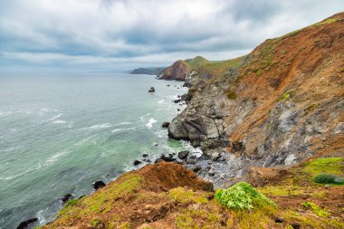 Marin Headlands, Kaliforniya 'daki Rodeo Sahili Sahil Yolu' ndan manzara, engebeli uçurumları, gizli sahil koylarını ve San Francisco yakınlarında bulutlu gökyüzünün altında Pasifik Okyanusu 'nu gösteriyor.