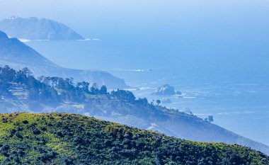 Garrapata Eyalet Parkı 'ndaki Soberanes Canyon Trailhead' in sahil manzarası. Yuvarlanan yeşil tepeler mavi Pasifik Okyanusuyla buluşuyor. Deniz yığınları ve kayalıklar kıyı sisinin içinde kayboluyor.