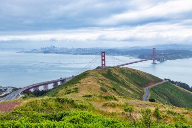 San Francisco Körfezi 'ni kaplayan Golden Gate Köprüsü' nün panoramik manzarası. Şehir manzarası, yemyeşil tepeler ve tekneler bulutlu bir bahar gününde yüksek bir noktadan çekiliyor.