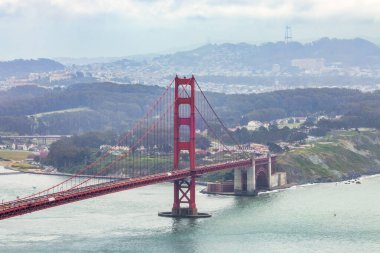 San Francisco Körfezi 'ni kaplayan Golden Gate Köprüsü' nün panoramik manzarası. Şehir manzarası, yemyeşil tepeler ve tekneler bulutlu bir bahar gününde yüksek bir noktadan çekiliyor.