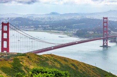 San Francisco Körfezi 'ni kaplayan Golden Gate Köprüsü' nün panoramik manzarası. Şehir manzarası, yemyeşil tepeler ve tekneler bulutlu bir bahar gününde yüksek bir noktadan çekiliyor.
