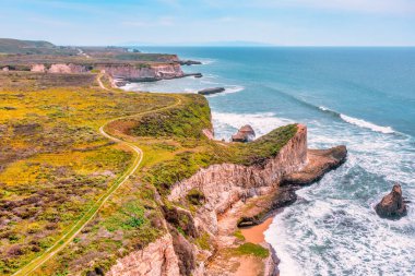 Kaliforniya, Davenport yakınlarındaki dramatik deniz kayalıkları boyunca kıyı şeridi kıvrımları var. Havadan bakıldığında, turkuaz üzerinde doğal bir kaya kemeri görünüyor. Pasifik kıyısındaki ikonik otoyol boyunca dalgalar var..