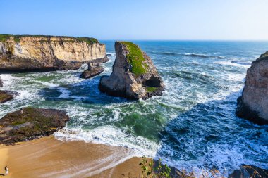 Davenport, California yakınlarındaki Iconic Shark Fin Cove, yukarıdan ele geçirildi. Dramatik kaya oluşumları, deniz mağarası ve okyanus dalgaları parlak mavi gökyüzünün altında engebeli kıyı şeridiyle buluşuyor.