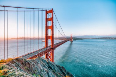 Golden Gate Köprüsü, San Francisco, California 'da gün doğumunda. Yumuşak pastel gökyüzü, sakin körfez suları ve ikonik kırmızı mimarisi olan Battery Spencer 'dan manzara. Huzurlu seyahat manzarası.
