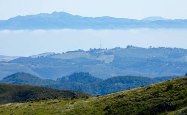 Kaliforniya 'da Soberanes Kanyonu yakınlarındaki Toro Dağı ve katmanlı yeşil tepelerin uzak manzarası, 1. Otoyol ve dağların altında süzülen kıyı sisi.