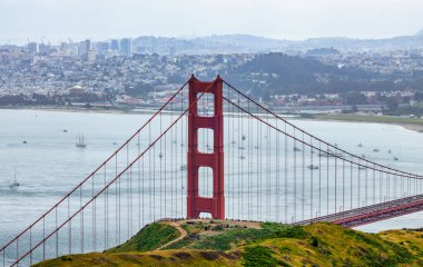 San Francisco Körfezi 'ni kaplayan Golden Gate Köprüsü' nün panoramik manzarası. Şehir manzarası, yemyeşil tepeler ve tekneler bulutlu bir bahar gününde yüksek bir noktadan çekiliyor.